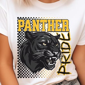 Pu&ograve; includere: Una t-shirt bianca con una stampa grafica di una testa di pantera nera con occhi gialli e denti in vista. Il design include il testo "PANTHER PRIDE" in lettere gialle, posizionato su uno sfondo quadrato a pois neri e gialli.