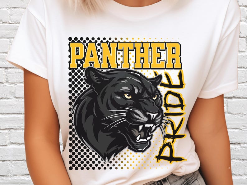 Pu&ograve; includere: Una t-shirt bianca con una stampa grafica di una testa di pantera nera con occhi gialli e denti in vista. Il design include il testo "PANTHER PRIDE" in lettere gialle, posizionato su uno sfondo quadrato a pois neri e gialli.