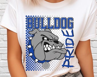 Può includere: Una t-shirt bianca con una stampa grafica di un bulldog grigio con un collare blu borchiato. Il testo BULLDOG è stampato in blu sopra il cane, e la parola PRIDE è stampata verticalmente in blu sulla destra. Il design include un motivo a pois.