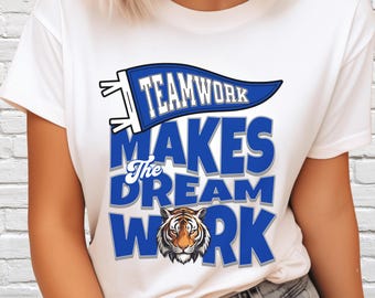 May include: White t-shirt with a blue and white graphic. The graphic reads "Teamwork Makes the Dream Work" with a tiger head at the bottom. The word "Teamwork" is on a blue pennant.