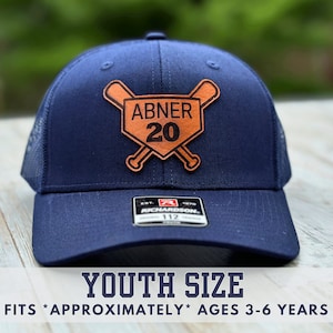 May include: A navy blue youth-sized baseball cap with a brown leather patch featuring a baseball diamond, crossed bats, and the name "ABNER 20".