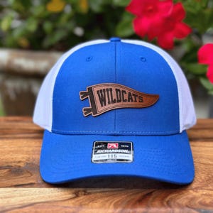 May include: A blue and white trucker hat with a brown leather patch that reads "Wildcats." The hat has a curved brim and a mesh back. The Richardson 115 tag is visible on the front.