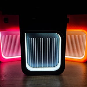 May include: Three illuminated rectangular devices with a black frame. The centre device has a white and blue panel with vertical lines. The devices on either side glow red and orange. The background is dark.