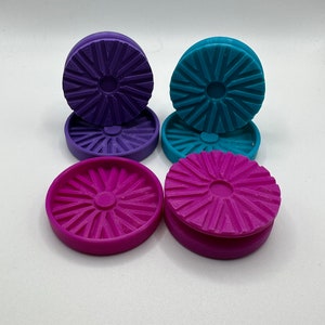 Puede incluir: Cuatro posavasos redondos de pl&aacute;stico de colores vivos con un dise&ntilde;o de estrella. Los posavasos est&aacute;n apilados en pares, con dos posavasos morados a la izquierda y dos posavasos azules a la derecha. El posavasos inferior de cada par es de un tono m&aacute;s oscuro del color.