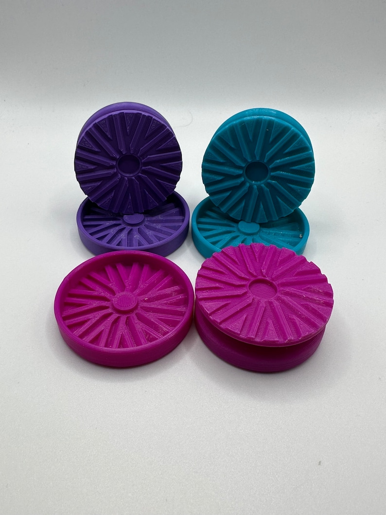 Puede incluir: Cuatro posavasos redondos de pl&aacute;stico de colores vivos con un dise&ntilde;o de estrella. Los posavasos est&aacute;n apilados en pares, con dos posavasos morados a la izquierda y dos posavasos azules a la derecha. El posavasos inferior de cada par es de un tono m&aacute;s oscuro del color.