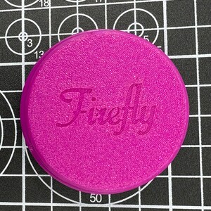 Puede incluir: Una tapa redonda de pl&aacute;stico de color magenta con la palabra "Firefly" impresa en blanco en letra cursiva.