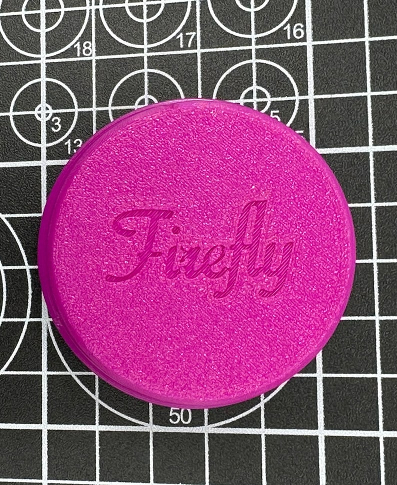 Puede incluir: Una tapa redonda de pl&aacute;stico de color magenta con la palabra "Firefly" impresa en blanco en letra cursiva.