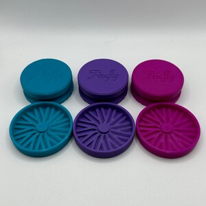 Puede incluir: Tres juegos de tapas redondas de pl&aacute;stico de colores con la palabra "Firefly" en relieve en la parte superior. Las tapas son de color turquesa, morado y rosa. Cada tapa tiene un dise&ntilde;o circular decorativo en la parte inferior.