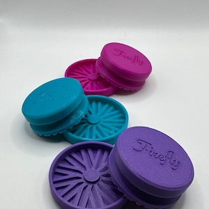 Puede incluir: Tres molinillos Firefly, uno morado, uno azul verdoso y uno rosa. Cada molinillo tiene un dise&ntilde;o circular con un agujero central y un borde elevado.