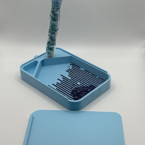 May include: A light blue diamond painting tray with a clear pen and a lid. The tray has a built-in grid and a section for holding diamonds. The lid is a flat surface with a small groove for holding the pen. The tray has the word "Freely" printed on the side.