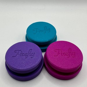 Puede incluir: Tres recipientes redondos apilables con la palabra "Firefly" en relieve en la parte superior. Los recipientes son de color turquesa, morado y rosa.