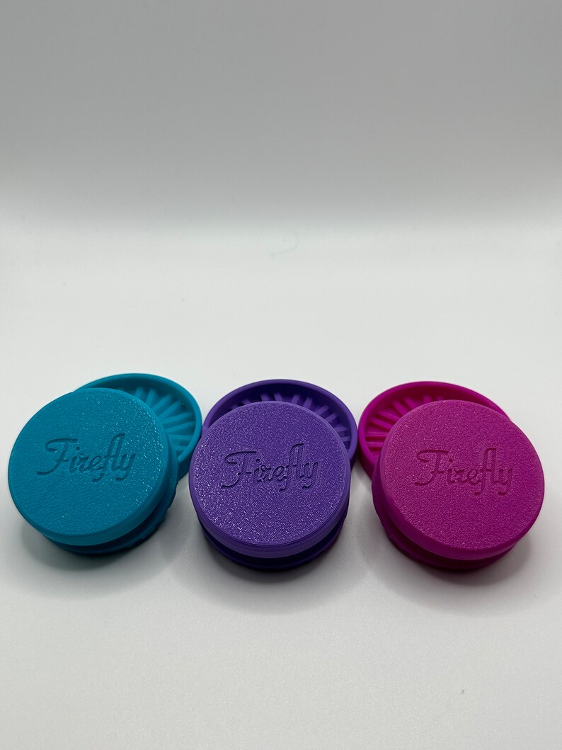 Puede incluir: Tres tapas de silicona con la palabra "Firefly" en relieve en la parte superior. Las tapas son de color turquesa, morado y rosa.