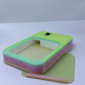 K&ouml;nnte beinhalten: Ein rechteckiges Ger&auml;t in Neongr&uuml;n und Pink mit hellgr&uuml;nem Innenraum und Boden. Das Ger&auml;t hat einen Schalter oben und das Wort "Firefly" ist auf der Seite aufgedruckt. Ein kleiner, hellbrauner Stab liegt auf dem Boden.