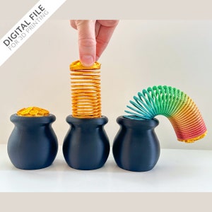May include: Three black pots with gold coin lids, each holding a different coloured spring toy. The first pot has a gold spring, the second has a rainbow spring, and the third has a green spring.