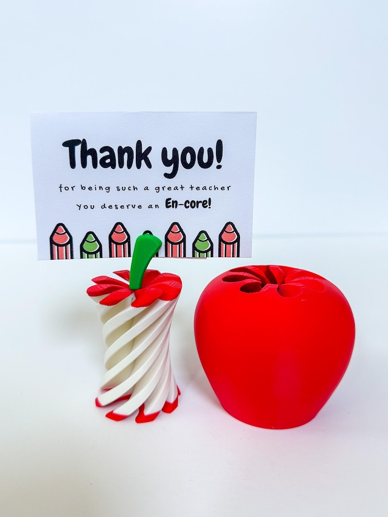 May include: A red apple-shaped pencil holder and a white and red pencil-shaped holder are displayed next to a card that says "Thank you!" in black text. The card also says "for being such a great teacher You deserve an En-core!"