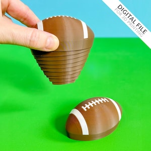 May include: Two brown football-shaped objects with white stripes and stitching. One is held by a hand, the other rests on a green surface. The text "DIGITAL FILE FOR 3D PRINTING" is in the upper right corner.