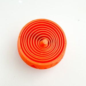 Pu&ograve; includere: Giocattolo di plastica arancione con cerchi concentrici, che ricorda un bersaglio o una trottola.