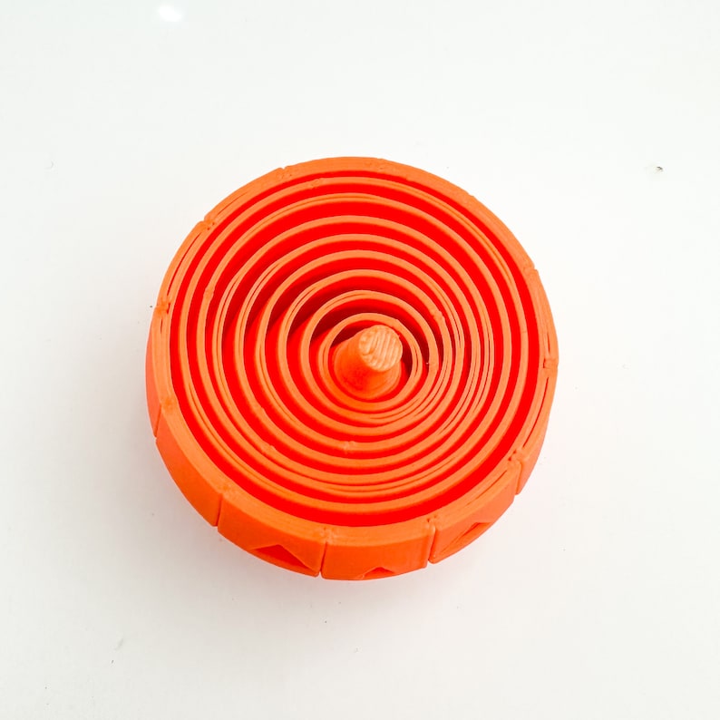 Pu&ograve; includere: Giocattolo di plastica arancione con cerchi concentrici, che ricorda un bersaglio o una trottola.