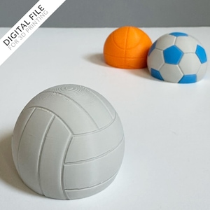 May include: Three 3D-printed sports balls: a grey volleyball, an orange basketball, and a football with white and blue panels. The volleyball is in the foreground, with the basketball and football behind it. Text in the upper left corner reads "DIGITAL FILE FOR 3D PRINTING."