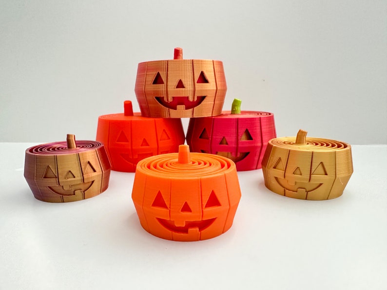 Pu&ograve; includere: Cinque contenitori a forma di zucca di Halloween di colore arancione, rosso e oro con un viso sorridente intagliato. I contenitori sono impilati uno sopra l'altro.