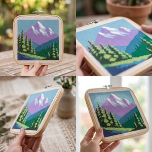 May include: A square cross-stitch embroidery piece featuring a mountain landscape with a purple mountain peak, white snow caps, and dark green pine trees. The fabric is mounted in a light-colored wooden square embroidery hoop with a metal tension screw.