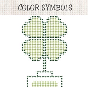 May include: A cross-stitch pattern chart titled COLOR SYMBOLS featuring a four-leaf clover design. The clover is outlined in dark green heart icons and filled with light green coffee cup symbols. A rectangular base is also outlined in dark green hearts.