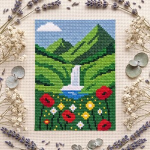 Pu&ograve; includere: Un ricamo a punto croce che raffigura un paesaggio con montagne verdi, una cascata bianca e una pozza blu. Il primo piano presenta papaveri rossi e fiori di campo gialli e bianchi sotto un cielo azzurro con una singola nuvola bianca.