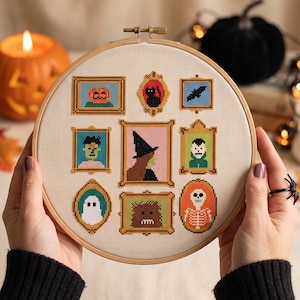 May include: A circular wooden embroidery hoop containing a cross-stitch pattern of nine framed Halloween icons, including a pumpkin, black cat, bat, ghost, witch, skeleton, and various monsters, all stitched on a light beige fabric background.