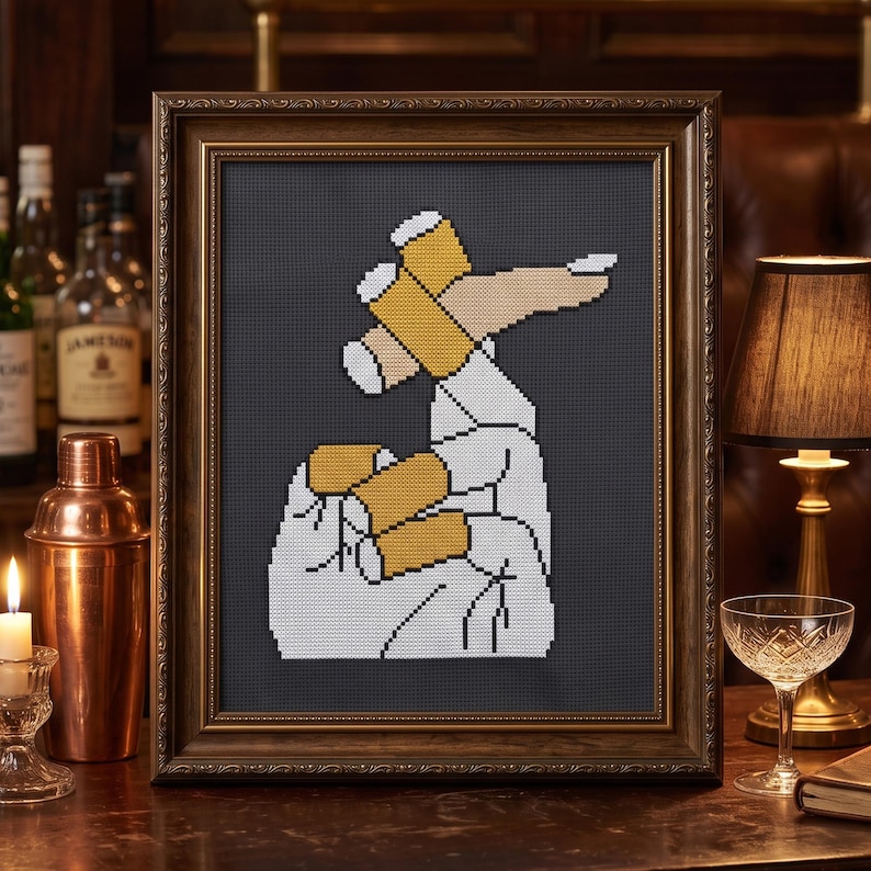 Pu&ograve; includere: Un ricamo a punto croce incorniciato che presenta una grafica pixelata di una mano che tiene tre sigarette. Il design utilizza filo bianco, beige e giallo su uno sfondo grigio scuro, racchiuso in una cornice decorativa in legno marrone scuro.