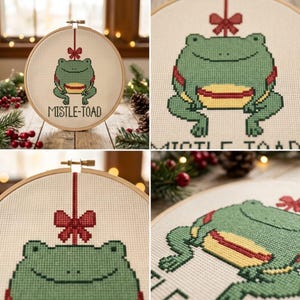 May include: A circular wooden embroidery hoop containing a cross-stitch design of a green frog with a yellow belly, suspended by a red ribbon with a bow. The text MISTLE-TOAD is stitched in black below the frog on a cream-colored fabric background.