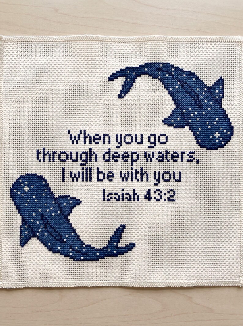May include: A square cross-stitch embroidery on off-white fabric featuring two dark blue whale sharks with white spots. The text in the centre reads: When you go through deep waters, I will be with you Isaiah 43:2, stitched in dark blue thread.