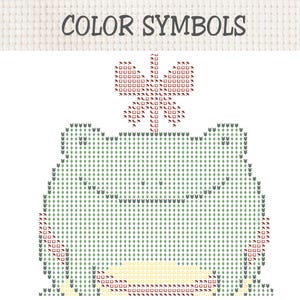 May include: A cross-stitch pattern chart titled COLOR SYMBOLS featuring a grid design of a frog with a butterfly on its head. The frog is composed of light green diamond symbols, while the butterfly uses red square and umbrella icons.
