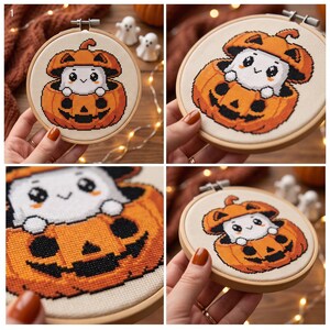 May include: A circular wooden embroidery hoop containing a cross-stitch pattern of a white ghost character with large black eyes sitting inside a carved orange jack-o'-lantern pumpkin. The design is stitched on a light beige fabric background.