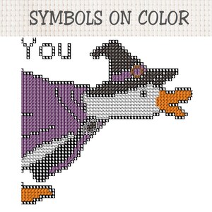 Op de afbeelding: Een kruissteekpatroon getiteld SYMBOLS ON COLOR met een eend die een zwarte heksenhoed met een paarse band draagt. De eend heeft een witte kop, een oranje snavel en een paars lichaam. Het ontwerp bevat het woord YOU in zwarte omlijnde letters.