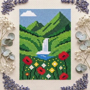 Pu&ograve; includere: Un ricamo a punto croce che raffigura un paesaggio con montagne verdi, una cascata bianca e un cielo azzurro con una nuvola bianca. Il primo piano presenta un campo di papaveri rossi, fiori gialli e piccoli fiori bianchi su un tessuto.