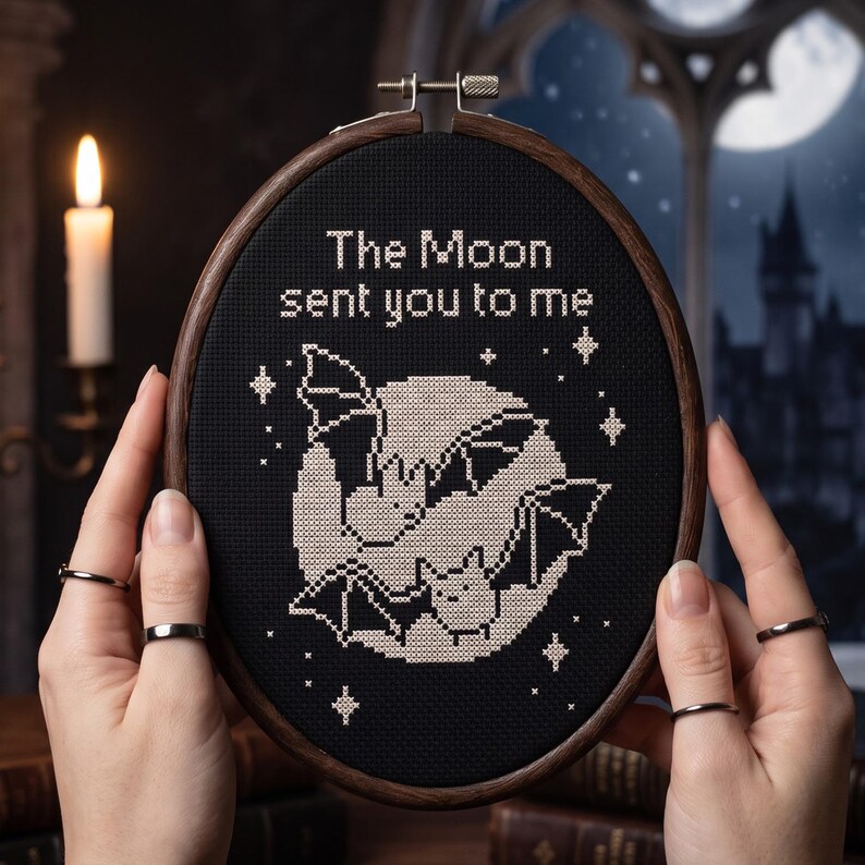Puede incluir: Un bastidor de bordado ovalado con tela negra y bordado de punto de cruz blanco. El dise&ntilde;o muestra dos murci&eacute;lagos volando frente a una luna grande, rodeados de estrellas peque&ntilde;as. El texto dice "The Moon sent you to me" en hilo blanco.