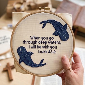 May include: A circular wooden embroidery hoop containing cream-coloured fabric with a cross-stitch design of two dark blue whale sharks and the text: When you go through deep waters, I will be with you Isaiah 43:2, stitched in dark blue thread.