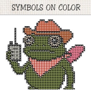 May include: A cross-stitch pattern featuring a green frog wearing a brown cowboy hat and a red bandana, holding a gray rectangular device with an antenna. The text SYMBOLS ON COLOR is printed at the top of the grid-based design.