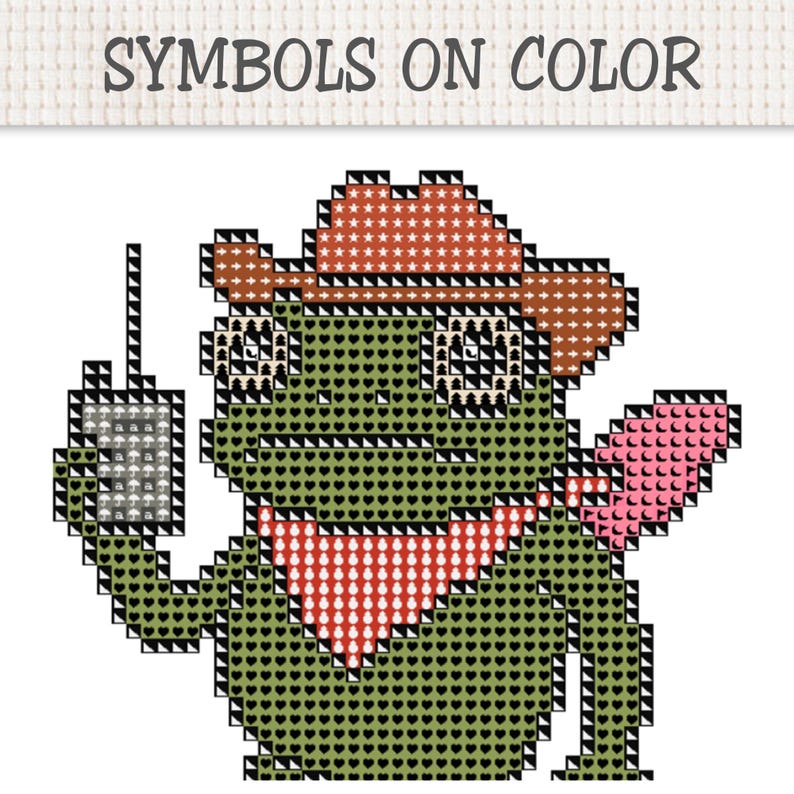 May include: A cross-stitch pattern featuring a green frog wearing a brown cowboy hat and a red bandana, holding a gray rectangular device with an antenna. The text SYMBOLS ON COLOR is printed at the top of the grid-based design.