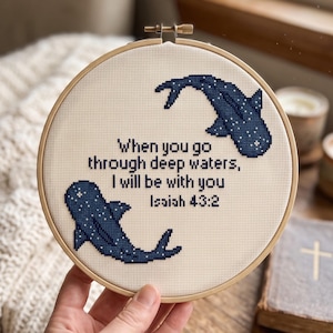 May include: A circular wooden embroidery hoop containing a cross-stitch design on cream-coloured fabric. The design features two dark blue whale sharks with white spots and the text: When you go through deep waters, I will be with you Isaiah 43:2.