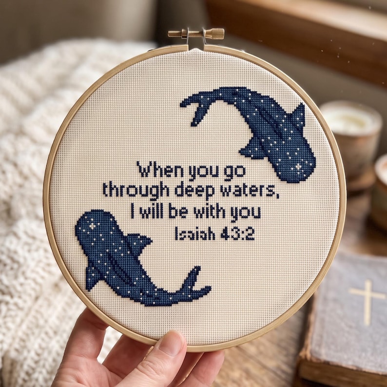 May include: A circular wooden embroidery hoop containing a cross-stitch design on cream-coloured fabric. The design features two dark blue whale sharks with white spots and the text: When you go through deep waters, I will be with you Isaiah 43:2.