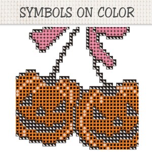 K&ouml;nnte beinhalten: Ein Kreuzstichmuster mit dem Titel SYMBOLS ON COLOR, das zwei orangefarbene K&uuml;rbisse mit schwarzen Gesichtsz&uuml;gen und Stielen zeigt, gekr&ouml;nt von rosa Bl&auml;ttern. Das Design verwendet ein Gitter aus schwarzen, orangen und rosa Stichen auf wei&szlig;em Grund.