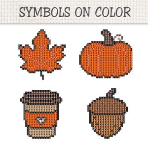 May include: A cross-stitch pattern sheet titled SYMBOLS ON COLOR featuring four autumn-themed designs: a maple leaf, a pumpkin, a coffee cup, and an acorn. Each icon is composed of a grid of colored squares filled with alphanumeric symbols.