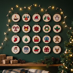 Pode incluir: Vinte bastidores de bordado circulares de madeira dispostos numa grelha, cada um contendo um design de ponto cruz em estilo pixel-art de &iacute;cones de Natal, incluindo uma vela, ornamentos, gorro de Pai Natal, boneco de neve e &aacute;rvore.