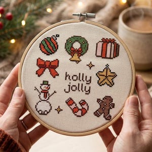 May include: A round wooden embroidery hoop containing a cream-colored fabric with cross-stitch designs of a striped ornament, a wreath, a gift, a red bow, a yellow star, a snowman, a candy cane, and a gingerbread man with the text holly jolly.
