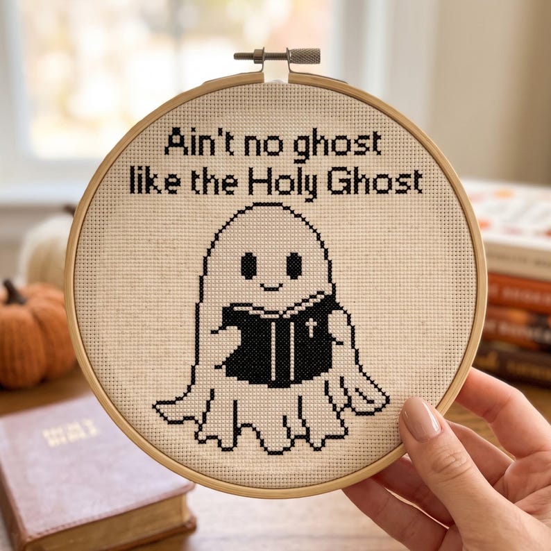 May include: A circular wooden embroidery hoop containing a piece of cream-coloured Aida fabric with black cross-stitch embroidery. The design features a cartoon ghost holding a black book with a cross, and the text: Ain't no ghost like the Holy Ghost.