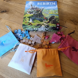 Op de afbeelding: Een bordspel genaamd "Rebirth" met een kleurrijke doos en vijf kleine trekzakjes. De zakjes zijn blauw, wit, oranje, rood en bruin. De zakjes bevatten kleine houten spelstukken.