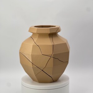 Pu&ograve; includere: Un vaso in ceramica marrone chiaro con un design geometrico e crepe su tutta la superficie. Il vaso &egrave; posto su un piedistallo bianco.