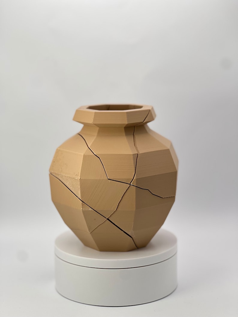 Pu&ograve; includere: Un vaso in ceramica marrone chiaro con un design geometrico e crepe su tutta la superficie. Il vaso &egrave; posto su un piedistallo bianco.