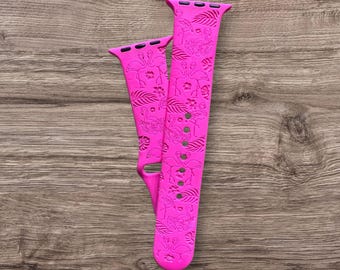 May include: Two vibrant pink watch straps featuring a flamingo and tropical leaf design. The straps are made of a flexible material and have adjustment holes. The design is etched into the surface, creating a textured effect.
